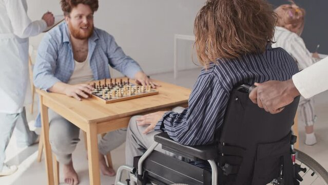 Unrecognizable medical worker bringing man with mental disorder to fellow patient, they starting to play chess
