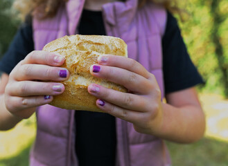 Young girl is holding a fresh wheat bun from a bakery in her hands. Image for bakery products or unhealthy eating