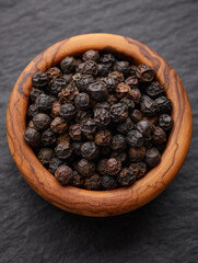 Black pepper in wooden bowl over black stone surface