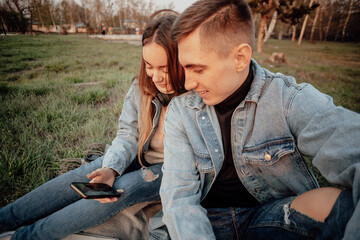 A young fashionable couple of students smiles while looking at the phone in the park