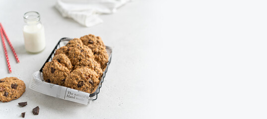 Bakery banner. Healthy oatmeal cookies in basket and a bottle of milk on light concrete background....