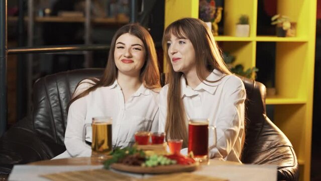 Two beautiful girls in a bar at a table are looking at guys and flirting and courting
