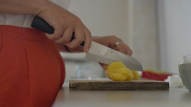 Static, close up of a woman cutting potatoes with a chef knife in a tiny kitchen during midday. Panasonic Lumix S5 with a 75mm lens.