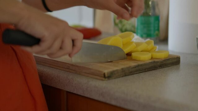 Close up of a woman slicing potatoes with a chef knife in a small kitchen with natural light. Panasonic Lumix S5 with a 75mm lens.