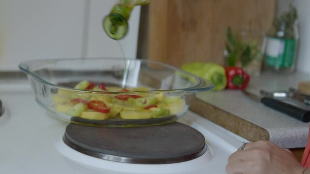 Close up shot of a woman pouring olive oil in a baking tray, in a small kitchen with natural light. Panasonic Lumix S5 with a 75mm lens.