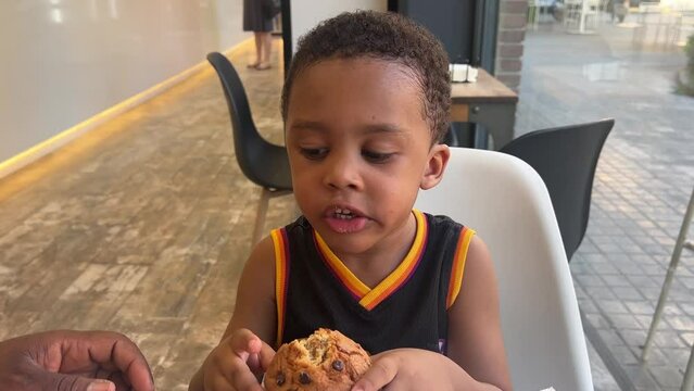 Cute 3-year-old black child eating a delicious muffin in a cafeteria