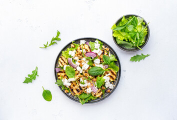 Delicious healthy salad with grilled zucchini, feta cheese, walnut, onion and spinach, white table background, top view