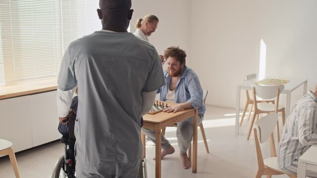 African American male nurse bringing patient with mental disorder to his friend, they starting chess game