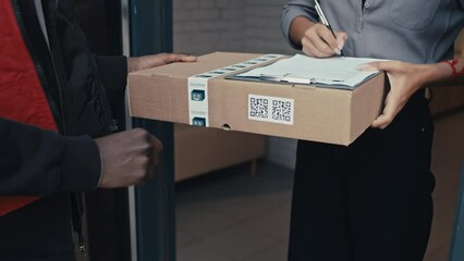 Close up shot of woman receiving package and signing off receipt, giving back to delivery man documents