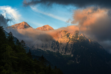 Great and dramatic view to the mountains of Slovenian Alps during sunrise on the border between Slovenia and Italy. Charming play of clouds with the morning sun light on the peaks.