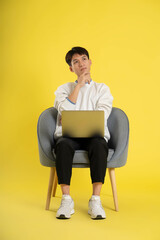 full body of young Asian man wearing sweater and using latop on yellow background