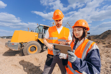 Team Engineers in hardhat use computer tablet for control unloading Industrial excavator. Concept...