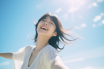 Side view of a Japanese girl with a huge smile on her face arms wide open with eyes closed enjoying a beautiful sunny day again a blue sky