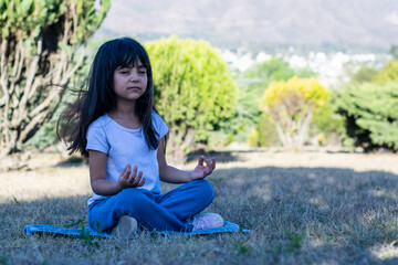 Niña latina al aire libre practicando yoga en un parque durante el día.