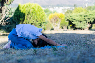 Niña practicando una pose de yoga al aire libre, en un parque con hermosos arbustos verdes.