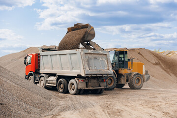Fototapeta premium Yellow Excavator loading sand to industrial truck on industry quarry. Construction site open pit mine concept