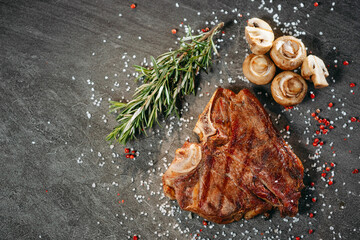 Cooked and grilled piece of juicy meat sitting on a sprinkle of salt and pepper peas, next to a sprig of rosemary and cooked mushrooms on a stone table