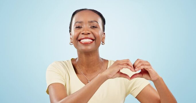 Heart, hands and face of black woman in studio for kindness, care and charity donation on blue background. Happy portrait, model and laugh for love, hope and thanks for support, emoji sign and peace