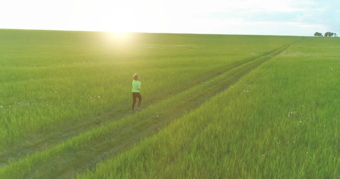 Aerial shoot of a sporty child runs through a wheat field. Evening sport training exercises at rural meadow. A happy childhood is a healthy way of life. Outdoor runing traning. Radial movement, sun