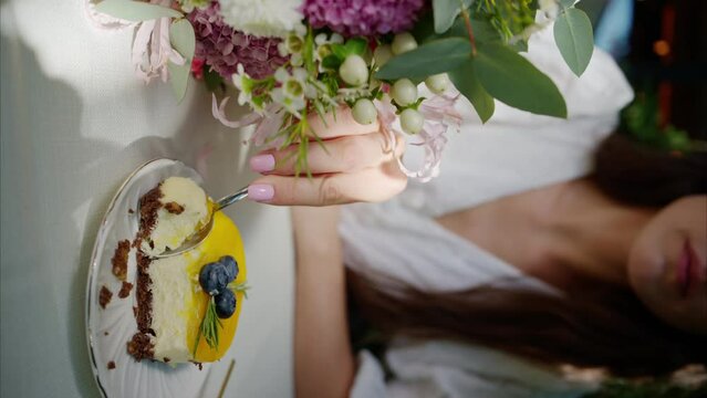 Woman eating yellow and chocolate cheese cake dessert at a terrace, composition with flowers, macaroons sweets desert and coffee and tea