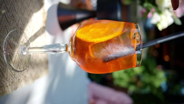 Woman hand stiring orange cocktail with orange and ice, slow motion