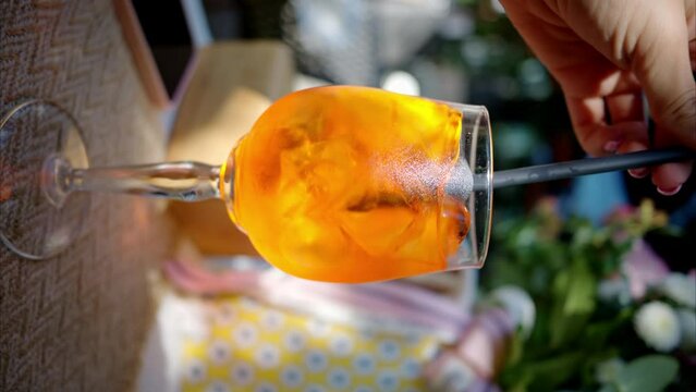 Woman hand stiring orange cocktail with orange and ice, slow motion