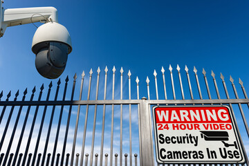Modern security camera monitoring the entrance to a gate of a private property with a sign with...