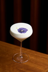Cocktail glass with white froth and purple flower petal.