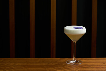 Cocktail glass with white froth and purple flower petal.