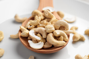 Raw nourishing cashew in kitchen wooden spoon on white ceramic surface