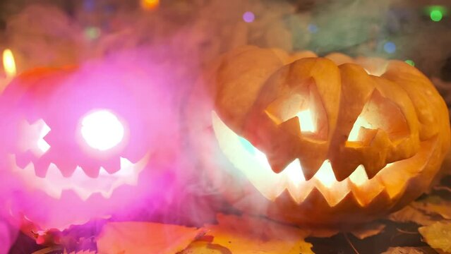 Close-up of two carved pumpkin lanterns amidst thick fog and smoke standing in the courtyard of a house during the Halloween celebration