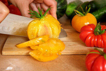 Woman using a knife cutting fresh raw vegetables. Tomatoes, cucumbers being sliced on a wooden board. Cooker at home making a healthy veggie meal. Chopping ingredients for preparing vegetarian dish
