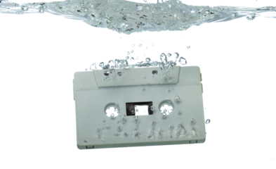 Cassette retro vintage Tape fall into clear water with air bubble. Black retro vintage cassette magnetic tape drop to wash old time. White background isolated freeze element