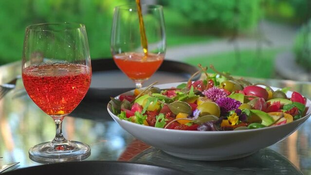 Lunch or dinner in a restaurant in the summer season. Pouring a aperol spritz alcohol beverage into glasses in a summer cafe. Delicious Italian alcoholic drink and fresh salad on the table