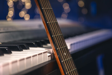 Guitar and piano keys close-up on a blurred background with bokeh. - obrazy, fototapety, plakaty