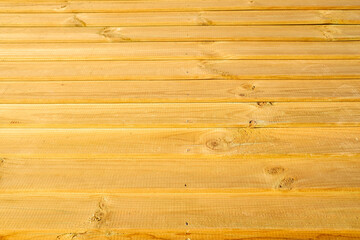 Bare wooden planks line a wall, in the yellow sun and weather.