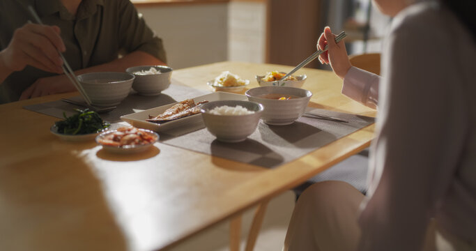 Couple Eating Delicious Korean Dinner with Chopsticks in the Kitchen at Home. Footage Focusing on Food on the Dining Table with Rice Bowls, Spicy Asian Soup, Fish and Vegetables