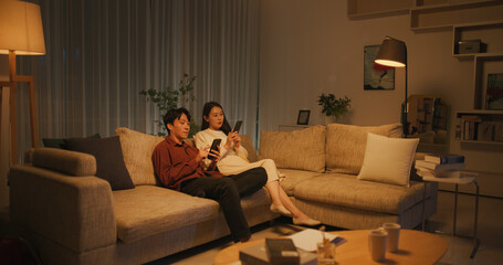 Young South Korean Couple Using Smartphones While Relaxing on a Couch at Home in a Stylish Living...