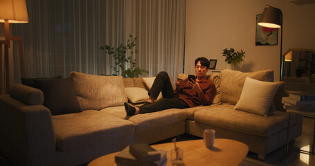 Young South Korean Man Using Online Shopping App in a Cozy Apartment, Making Secure Purchases with...