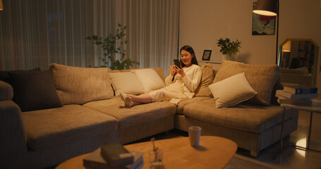 Young South Korean Woman Engaged and Connected Online, Enjoying Leisure Time with Her Smartphone, Spending Time Resting on a Sofa and Exploring Social Media and Entertainment Apps