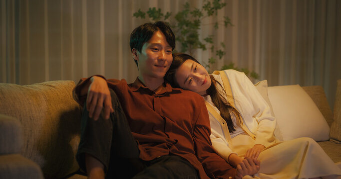 Portrait of a South Korean Couple Watching Romantic Comedy Movie on TV. Happy Boyfriend and Girlfriend Enjoying Funny Television Series Together at Home, Sitting Together on a Couch Late at Night