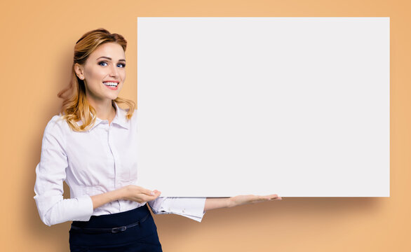 Happy excited smiling business woman in white confident clothing showing blank banner signboard. Success and advertising concept. Copy space empty place for some text. Brown beige background.