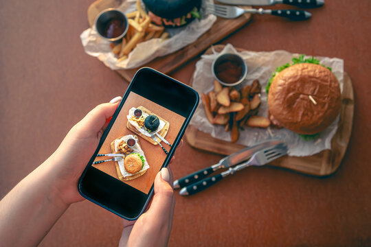 A woman takes pictures of burgers on her smartphone.