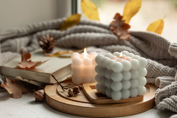 Home autumn composition with candles, leaves and knitted element.