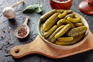 Pickled cucumbers with salt, pepper, garlic, and bay leaf. Fermented food. Homemade canned gherkins on a black slate background