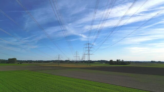 R&uuml;ckw&auml;rts Flug mit einer Drohne zwischen Hochspannungsleitungen von Sendemasten in l&auml;ndlicher Umgebung, die bis zum Horizont reichen
