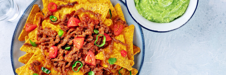 Nachos panorama, Mexican food, tortilla chips with beef and fresh vegetables and guacamole sauce, panoramic banner with copy space
