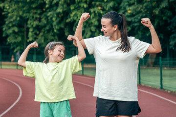 A woman and daughter are showing their biceps, working out at the stadium.