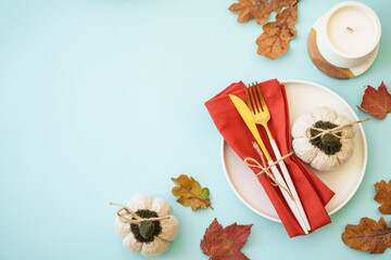 Thanksgiving table top view on blue background. White plate, cutlery and autumn decorations.