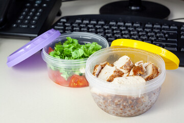Lunch on work place. Food box container with fresh salad, buckwheat and chicken on the working desk with keyboard.